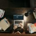 High-angle shot of a busy desk with books, laptop, and lamp, illustrating focused academia.