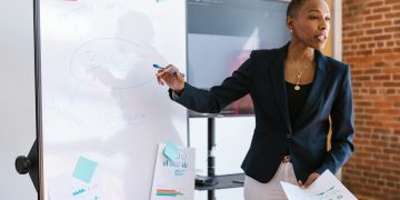 Professional businesswoman explaining budget strategy on a whiteboard during a meeting.