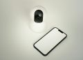 A smart home security camera paired with a blank smartphone on a white background.