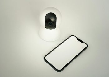 A smart home security camera paired with a blank smartphone on a white background.