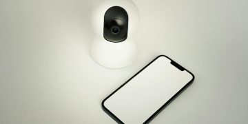 A smart home security camera paired with a blank smartphone on a white background.