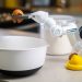 A robotic helper cracks an egg into a bowl in a contemporary kitchen setting, showcasing automation in cooking.