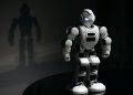 White robot toy casting a shadow in a dark studio setting, highlighting artificial intelligence.