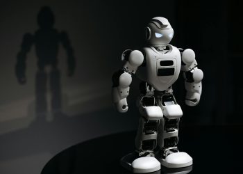 White robot toy casting a shadow in a dark studio setting, highlighting artificial intelligence.