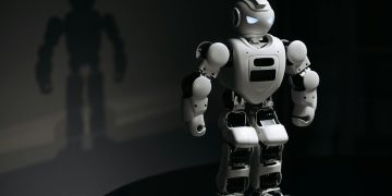 White robot toy casting a shadow in a dark studio setting, highlighting artificial intelligence.