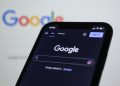 Smartphone screen showing Google search in dark mode with the Google logo in the background.