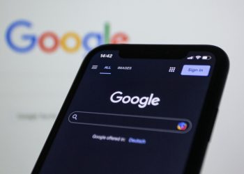 Smartphone screen showing Google search in dark mode with the Google logo in the background.