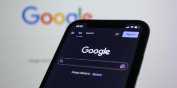Smartphone screen showing Google search in dark mode with the Google logo in the background.
