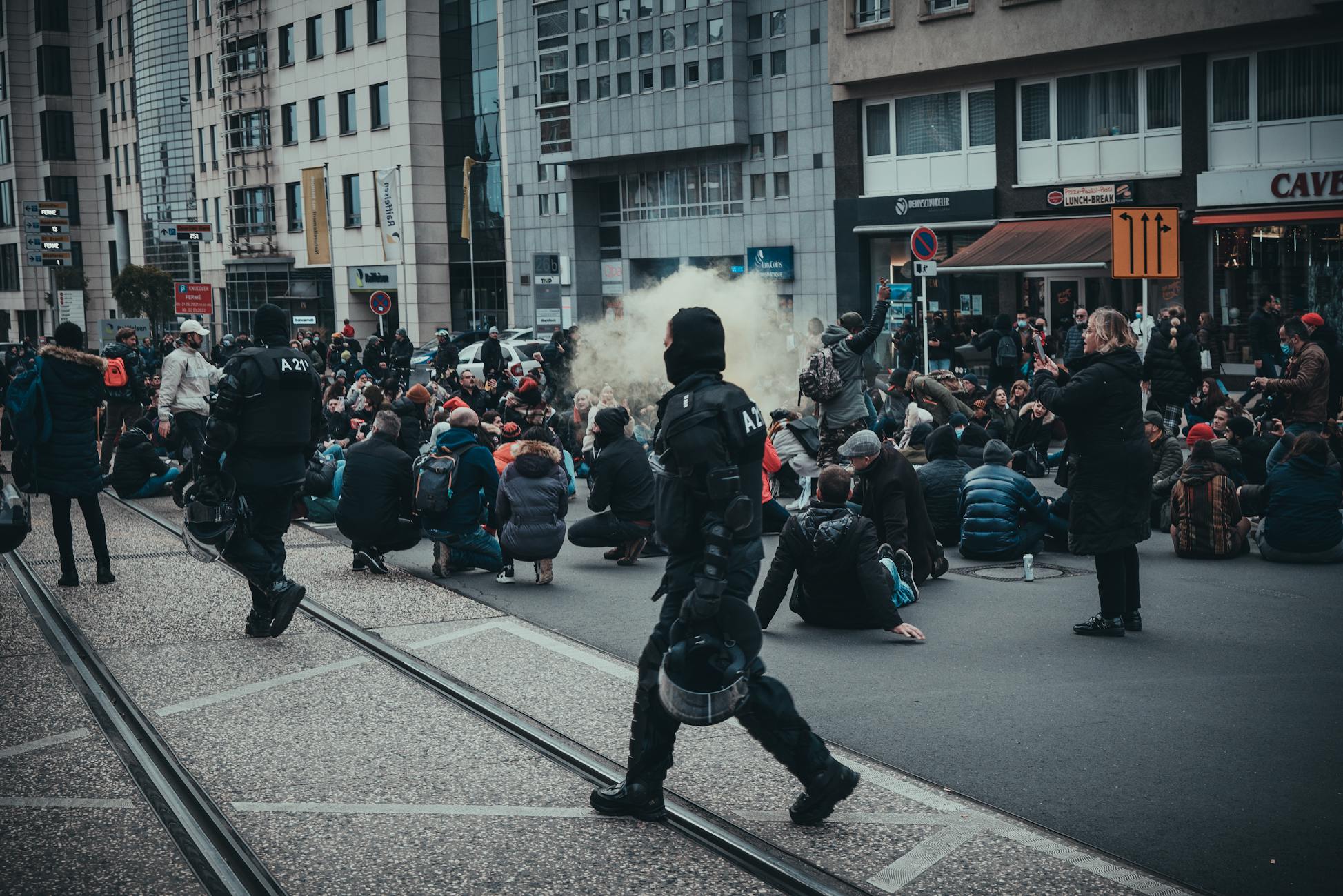Urban demonstration in Luxembourg City with police and seated protesters, creating a tense atmosphere.