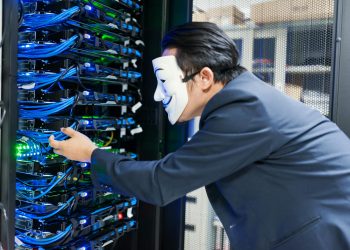 Masked individual interacting with server racks, symbolizing cybersecurity threats.
