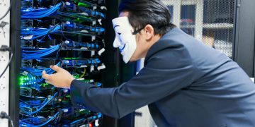 Masked individual interacting with server racks, symbolizing cybersecurity threats.