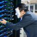 Masked individual interacting with server racks, symbolizing cybersecurity threats.