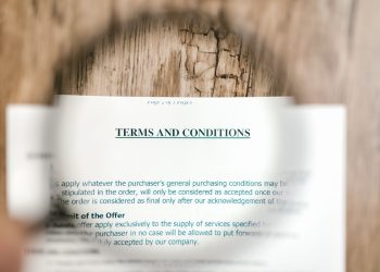 Magnifying glass focusing on terms and conditions document on wooden surface.