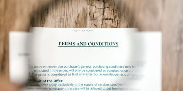 Magnifying glass focusing on terms and conditions document on wooden surface.