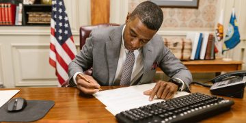 Professional man signs contract at desk in classic office environment.