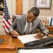 Professional man signs contract at desk in classic office environment.