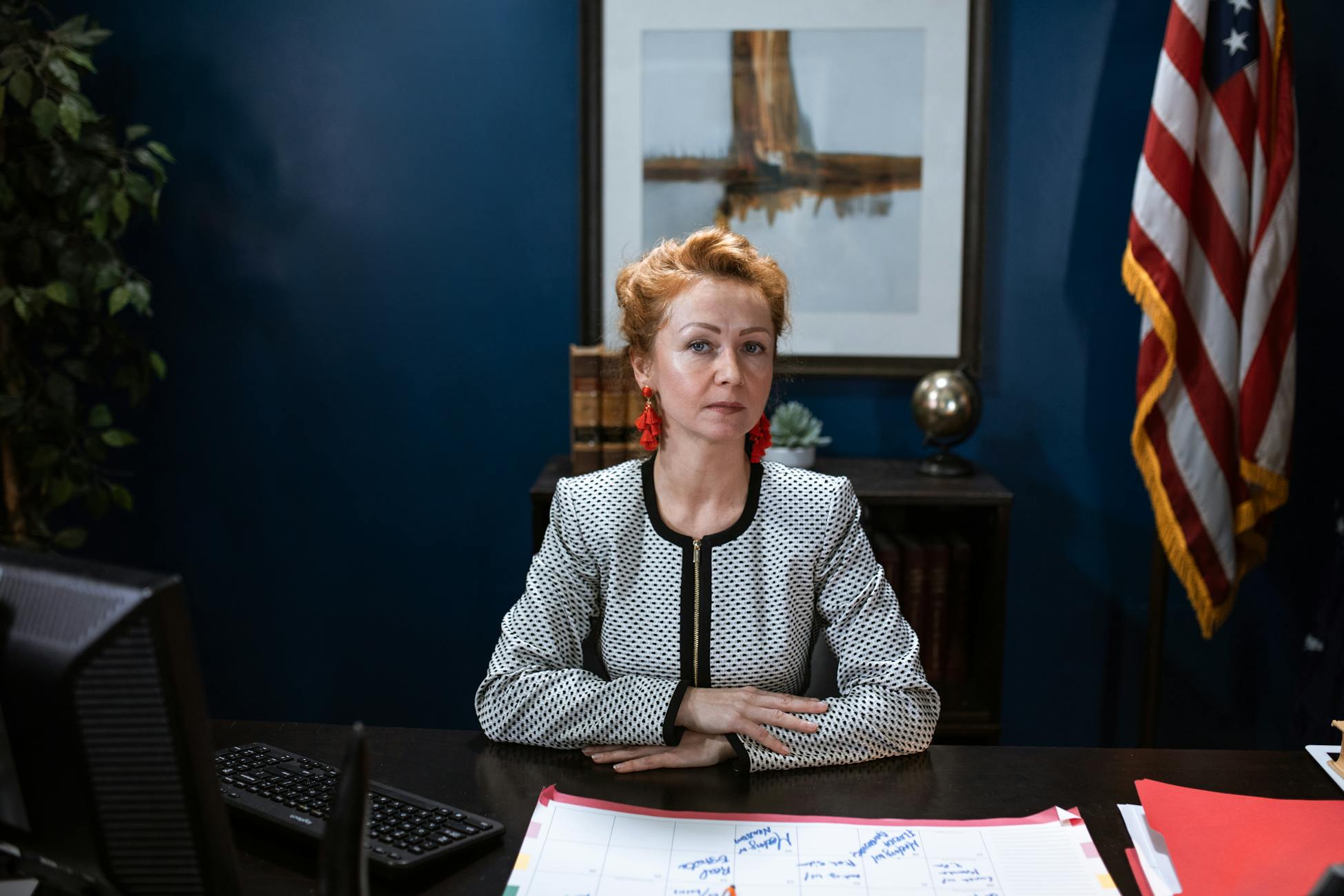 Confident woman in an office setting with a US flag behind her.