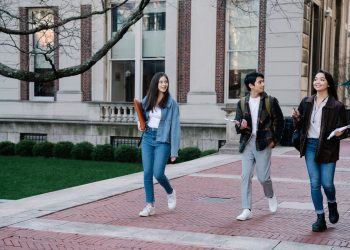 Group of young students walking on campus sidewalk on a bright day, showcasing casual university life.