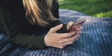A young woman using her smartphone while lying on a blanket outdoors.