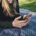 A young woman using her smartphone while lying on a blanket outdoors.