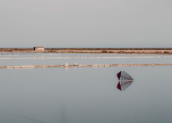 A tranquil scene of salt flats with still water reflecting structures under a clear sky.