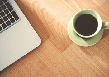 A coffee cup and laptop on a wooden desk, creating a cozy workspace vibe.