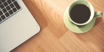 A coffee cup and laptop on a wooden desk, creating a cozy workspace vibe.