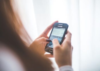 Close-up of a young woman typing on a Samsung smartphone at home. Bright indoor lighting.