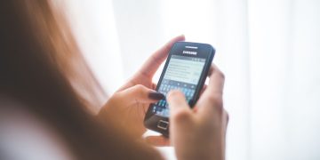 Close-up of a young woman typing on a Samsung smartphone at home. Bright indoor lighting.