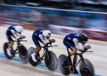 Three cyclists in motion racing on an indoor velodrome, showcasing speed and teamwork.