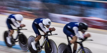 Three cyclists in motion racing on an indoor velodrome, showcasing speed and teamwork.