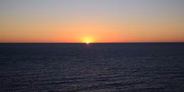 A tranquil sunset over a vast ocean horizon, showcasing vibrant colors and calm waters.