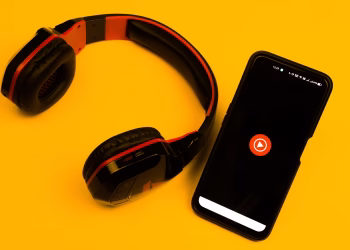 Wireless headphones and smartphone with play icon on a vibrant yellow background.