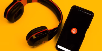 Wireless headphones and smartphone with play icon on a vibrant yellow background.