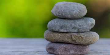 Four smooth stones stacked outdoors, symbolizing balance and tranquility.