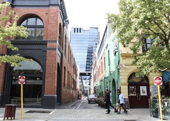 People walking in urban street with mix of historic and modern buildings.