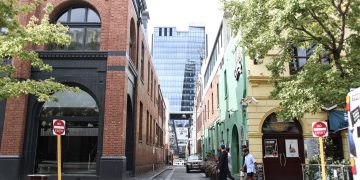 People walking in urban street with mix of historic and modern buildings.