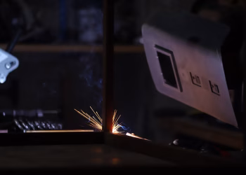 Close-up of a welding process in a dark workshop showing bright sparks and protective gear.