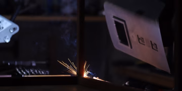 Close-up of a welding process in a dark workshop showing bright sparks and protective gear.