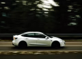 Dynamic shot of a white car in motion along a tree-lined highway capturing speed and elegance.