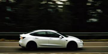 Dynamic shot of a white car in motion along a tree-lined highway capturing speed and elegance.