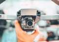 Crop unrecognizable person holding contemporary drone against blurred interior and demonstrating powerful camera