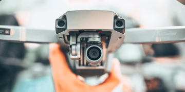 Crop unrecognizable person holding contemporary drone against blurred interior and demonstrating powerful camera