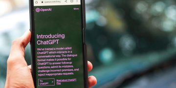 Close-up of a smartphone showing ChatGPT details on the OpenAI website, held by a person.