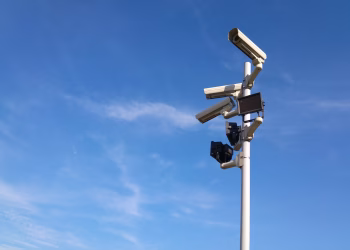 Multiple security cameras on a pole with a clear blue sky backdrop.