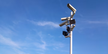 Multiple security cameras on a pole with a clear blue sky backdrop.