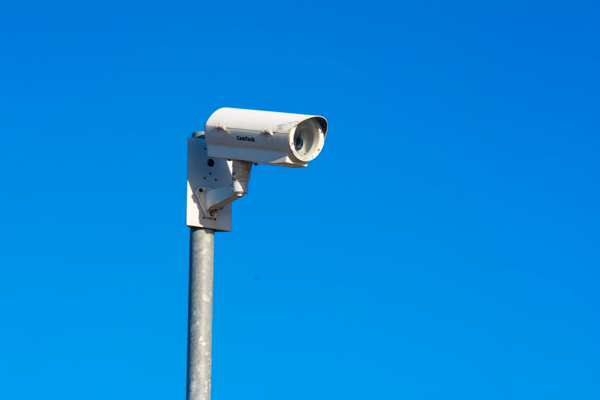 White security camera mounted on a pole under a clear blue sky, symbolizing security and surveillance.