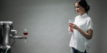 A robot presents a glass of wine to a woman, showcasing modern technology and interaction.