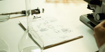 Close-up of a laboratory setup with documents, beaker, and microscope on a table.