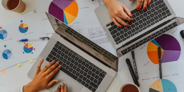 Overhead view of a team analyzing graphs and charts using laptops at a meeting.